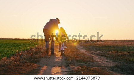 Dad teaches a little girl to ride a children's bike on the road in spring. Happy family. A father teaches his daughter to ride a bike in the park at sunset. Daddy and kid play together outdoors Royalty-Free Stock Photo #2144975879