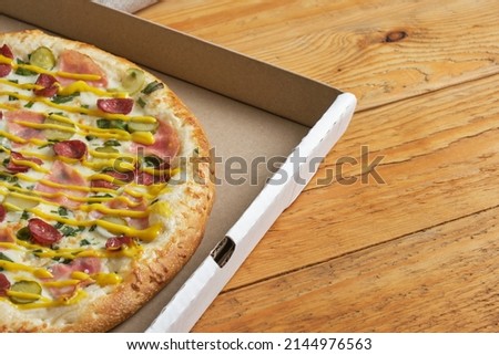 Hot Pizza in an open cardboard box. Tasty fresh pizza with cheese, sausage and tomatoes on a wooden background. Top view.