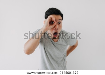 Funny obvious peeking Asian man in grey t-shirt isolated on white background. Royalty-Free Stock Photo #2145001399