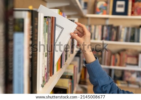 Female hand pulling book from bookshelf in public library in university, college or high school. Woman student take novel from bookcase in bookshop store, soft focus. Education and literature concept Royalty-Free Stock Photo #2145008677
