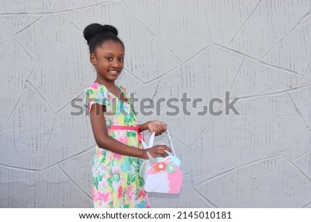 African American Girl smiling holding unicorn easter basket filled with eggs wearing colorful floral spring dress outdoors