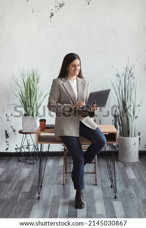 Full body confident business woman working on laptop and making online video conference at workplace in a trendy modern office. High quality photo