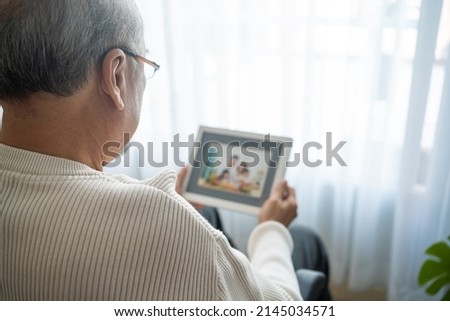 Asian senior male sit alone on wheelchair and looks family photographs. Elderly older mature grandfather feel lonely and sad, missing his relative and wife while stay in nursing home after retirement. Royalty-Free Stock Photo #2145034571