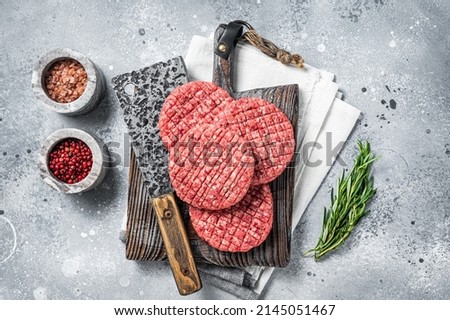 Raw beef meat burger patties on butcher wooden board with meat cleaver. Gray background. Top view.