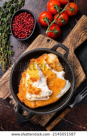 Roasted tilapia fillet in a skillet with breadcrumbs. Dark background. Top view.