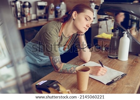 Tired female barista writing on clipboard in cafe Royalty-Free Stock Photo #2145060221