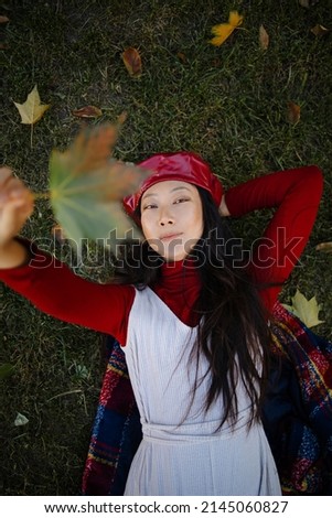 Autumn mood. Beautiful young asian woman in a leather hat lying on the autumn grass and yellow leaves. Seasonal autumn fashion.