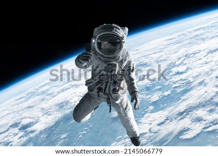 Female astronaut having a video call on her phone while performing space walk in open space, Earth in the background Royalty-Free Stock Photo #2145066779