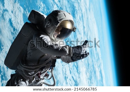 Female astronaut having a video call on her phone while performing spacewalk in open space, Earth in the background Royalty-Free Stock Photo #2145066785