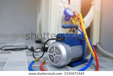 The back vacuum unit is placed beside the outdoor air conditioner unit and manifold gauge to use in servicing the air conditioner in the summer. Household appliance and electric appliance maintenance. Royalty-Free Stock Photo #2145071469