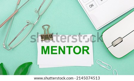 On a light green background there is a white calculator, a computer mouse, green leaves of a plant, gold-rimmed glasses and a white card with text MENTOR. Business concept