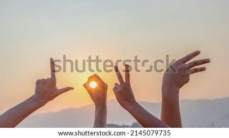 Hands is show letter L,O,V,E in sign language sunset background