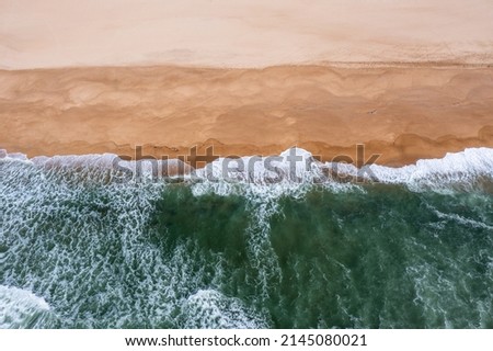 Top down drone view of whitecapped waves crashing on an empty golden sand beach