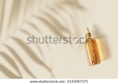 Liquid product packaging in glass bottle on pastel beige background and palm leaf shadow. Hyaluronic or polyglutamic acid oil cosmetic mock up. Facial cosmetics, minimal aesthetic trend, top view Royalty-Free Stock Photo #2145087375