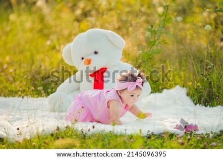 child sits next to a big teddy bear in nature