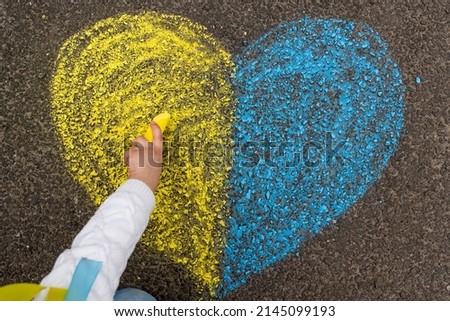 A child's hand draws a heart with crayons on the pavement with the patriotic national Ukrainian colors of yellow and blue. Stop the war in Ukraine. High quality photo