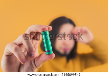Millennial dark-haired man showing battery to the camera yellow background copy space studio shot . High quality photo