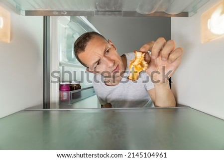 Man holds an apple core in his hand and looks at it in surprise. Hungry man is looking for food in the refrigerator. Photo from inside the refrigerator