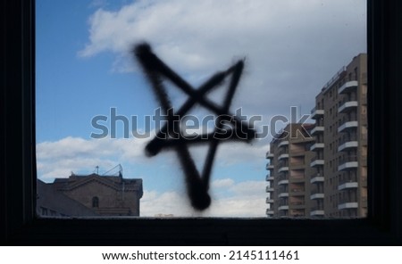 Reversed Pentagram symbol painted on dirty glass. black star on  blue  sky background. window frame. 