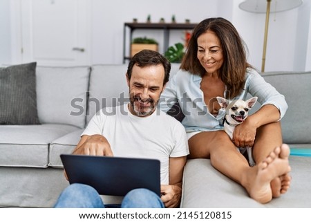 Middle age man and woman couple using laptop sitting on sofa with chihuahua at home