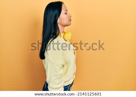 Beautiful hispanic woman with nose piercing wearing headphones on neck looking to side, relax profile pose with natural face with confident smile. 