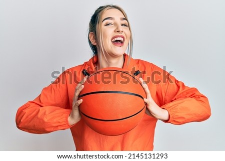 Young modern girl holding basketball ball smiling and laughing hard out loud because funny crazy joke. 