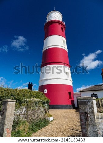 Red and white striped Happisburgh Lighthouse under blue sky and white clouds, Norfolk, UK