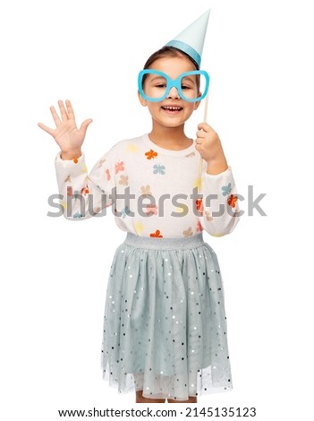 birthday, childhood and people concept - portrait of little girl in dress and party hat with glasses over white background