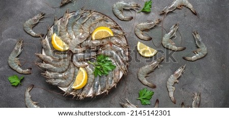 Raw tiger prawns with lemon and herbs on a dark grunge background. Fresh shrimps. Top view, flat lay, banner. Textured object, selective focus. Royalty-Free Stock Photo #2145142301