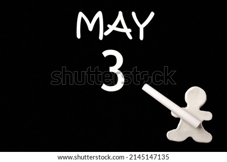 3rd day of May. A small white plasticine man writing the date 3 May on a black board. Business concept. Education concept. Spring month, day of the year concept.