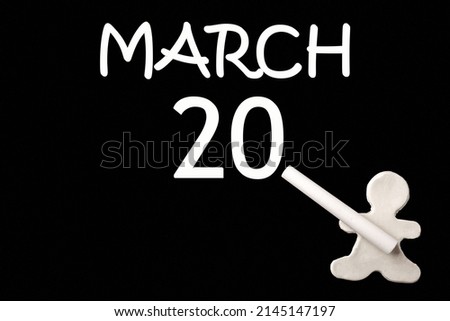 20th day of March. A small white plasticine man writing the date 20 March on a black board. Business concept. Education concept. Spring month, day of the year concept.