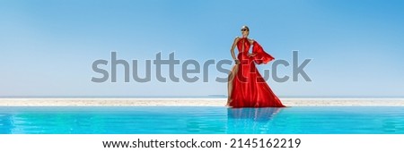Luxury fashion. Elegant fashion model. Stylish female model in red long gown dress on the Maldives beach. Elegance. Classy woman in amazing red dress near the pool. Couture. Vogue. Panorama. Royalty-Free Stock Photo #2145162219