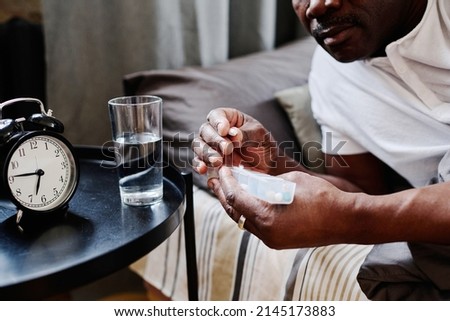 Hands of contemporary senior black man holding long plastic container with pills while taking medicaments after sleep in the morning Royalty-Free Stock Photo #2145173883