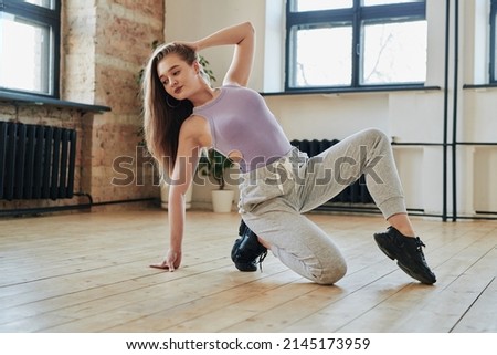 Blond teenage girl in tanktop and sweatpants performing new vogue dance movement on the floor of modern loft studio Royalty-Free Stock Photo #2145173959
