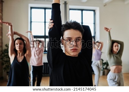 Confident teenage guy in black sweatshirt showing vogue dance movements to group of active teens standing behind Royalty-Free Stock Photo #2145174045