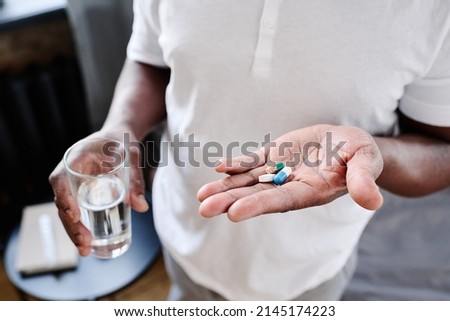 African American senior man with glass of water and three pills on hand going to take medicaments prescribed by his physician Royalty-Free Stock Photo #2145174223