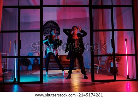 Couple of teenage dancers in posh apparel performing vogue dance movements while stnading in front of door of loft studio Royalty-Free Stock Photo #2145174261