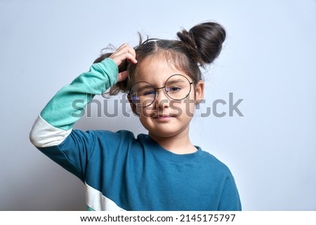 Funny little girl in glasses scratching her head doubts, makes decision isolated on yellow studio background Royalty-Free Stock Photo #2145175797