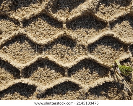 Brown ruffled sand surface with a diamond print - a trace of the tires of a car that has already passed (macro, horizontal, top view, texture).