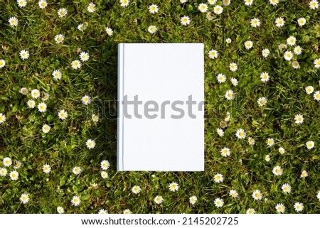 Book with a blank cover seen from above on a lawn with daisies. Royalty-Free Stock Photo #2145202725