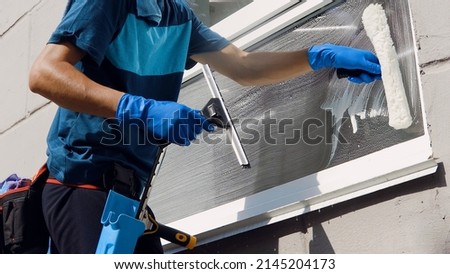 An employee of a professional cleaning service in overalls washes the glass of the windows of the facade of the building. Showcase cleaning for shops and businesses Royalty-Free Stock Photo #2145204173