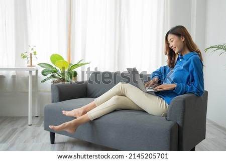 Young business freelance Asian woman working on laptop checking social media while lying on the sofa when relax in living room at home. Royalty-Free Stock Photo #2145205701