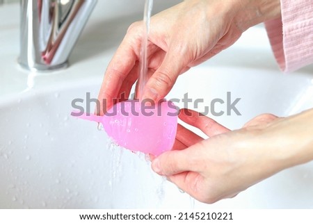 a young woman washes a menstrual cup in the bathroom Royalty-Free Stock Photo #2145210221