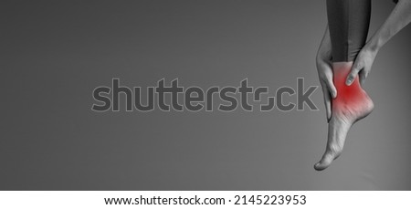 Banner with ankle pain. Woman holding painful leg. Injury, sprain, arthritis consequences. Health care, orthopedic problems and medicine concept. Black and white. Space for text. High quality photo Royalty-Free Stock Photo #2145223953