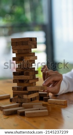 The girl's hand tried to pull out the wooden block without causing the tower to overturn. skill group game Construction business risk concept. Close-up photo with space for text next to it.