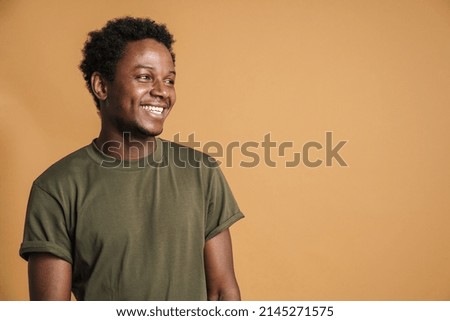 Young black man wearing t-shirt smiling and looking aside isolated over beige background