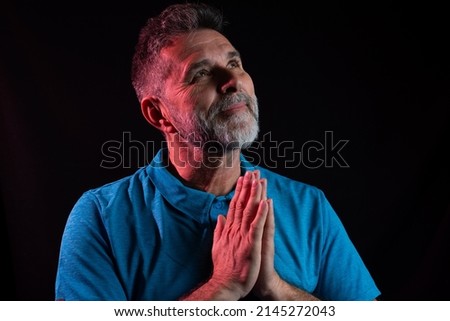 Closeup portrait mature man praying hands clasped hoping for best asking for forgiveness or miracle. Christian faith towards God concept. Concept for religion, faith, prayer and spirituality. Black.  Royalty-Free Stock Photo #2145272043