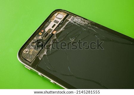 broken cell phone with shattered glass on green background. 