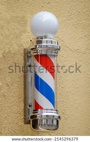 the classic symbol of a barber shop - barber's pole - in the form of a spiral of white, blue and red colors on the wall of the building in which the hairdresser is located