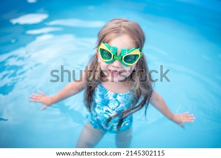 cute happy little girl in diving goggles and swimsuit. child learns to swim in the pool. training for children. concept kids sport, health, exercise, cooling in summer